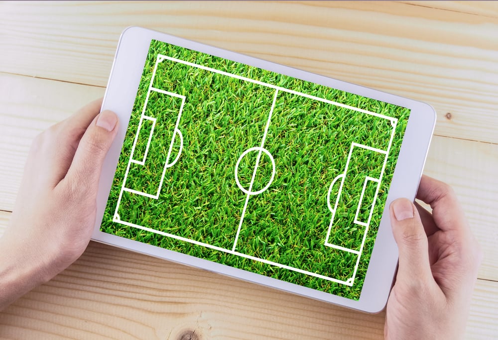 hands holding tablet showing football field image