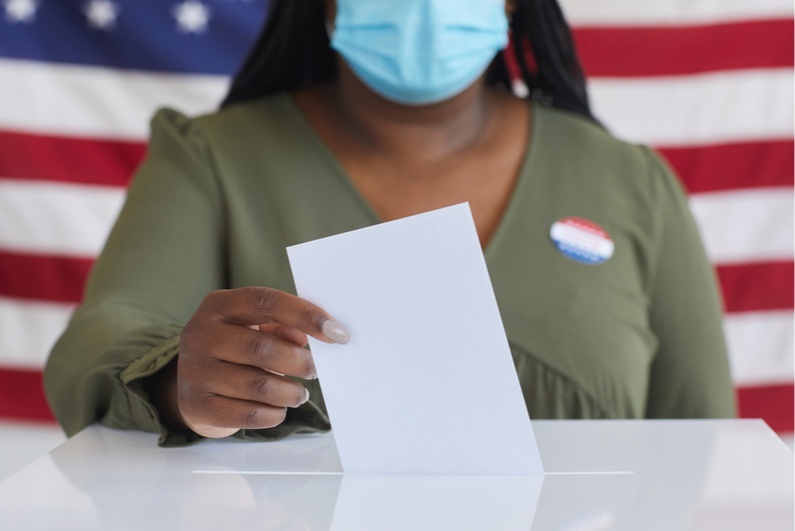 Woman wearing a protective mask placing a ballot in a ballot box