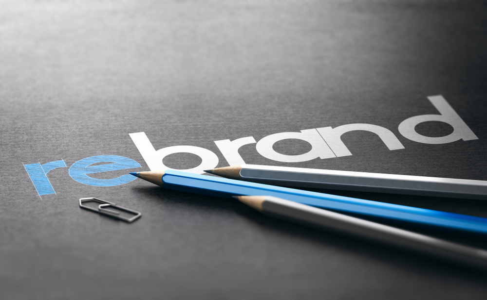 the word rebrand on a slate background, three pencils, and a paper clip